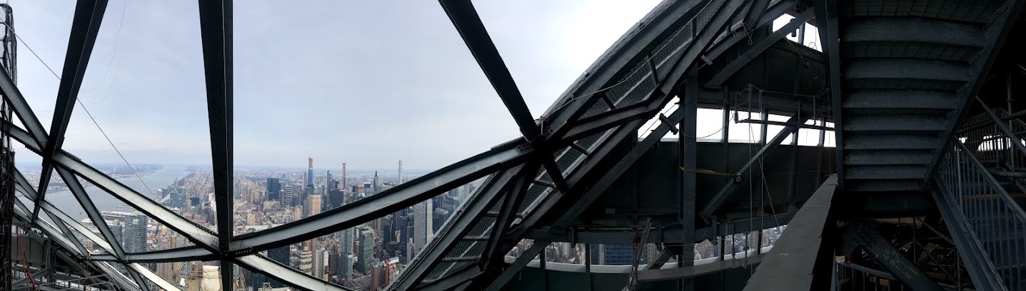 Panorama from inside the tower’s crown steel, with angled steel members framing the Hudson River and Manhattan skyline.