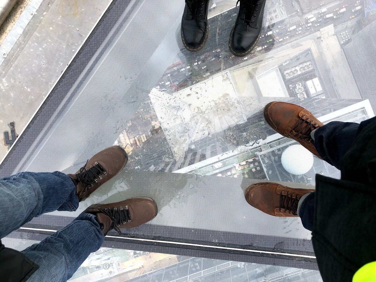 Looking down at several pairs of work boots on Edge’s glass floor during construction, with streets and rooftops visible far below.